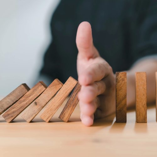 Geschaeftsperson stoppt fallende Dominosteine, Konzept für Risikomanagement und strategische Planung.