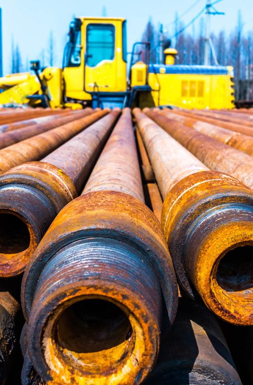 Gelber Bagger gelbgüter hinter Stapel von Stahlrohren auf Industriegelände