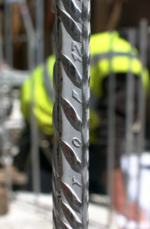 Detailaufnahme von Top12 Ferritische Stähle mit selektivem Fokus auf einer Baustelle, Bauarbeiter mit Schutzausrüstung unscharf im Hintergrund.