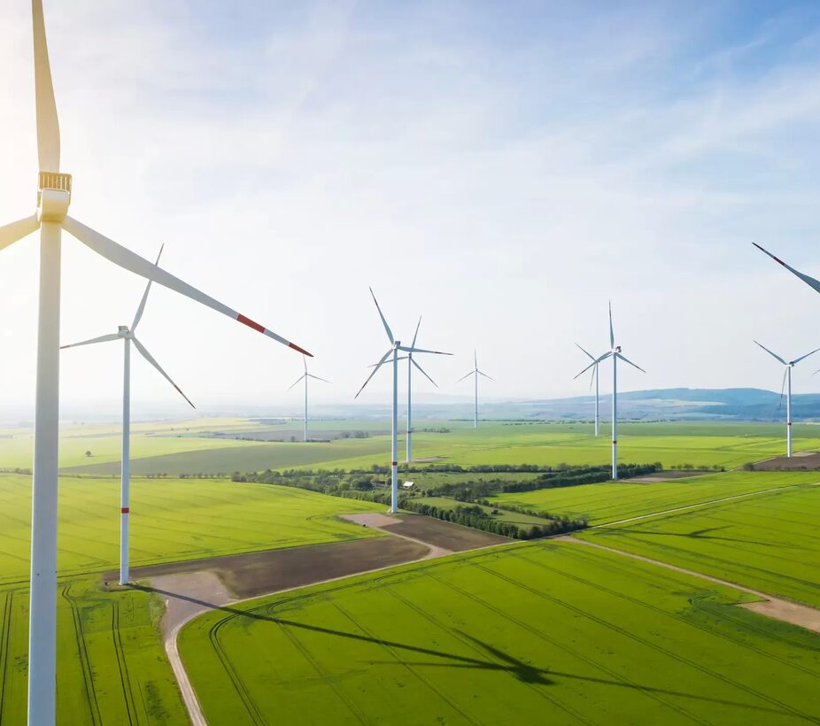 Luftaufnahme eines Windparks mit mehreren Windkraftanlagen auf einem grünen Feld für erneuerbare Energie und nachhaltige Entwicklung.